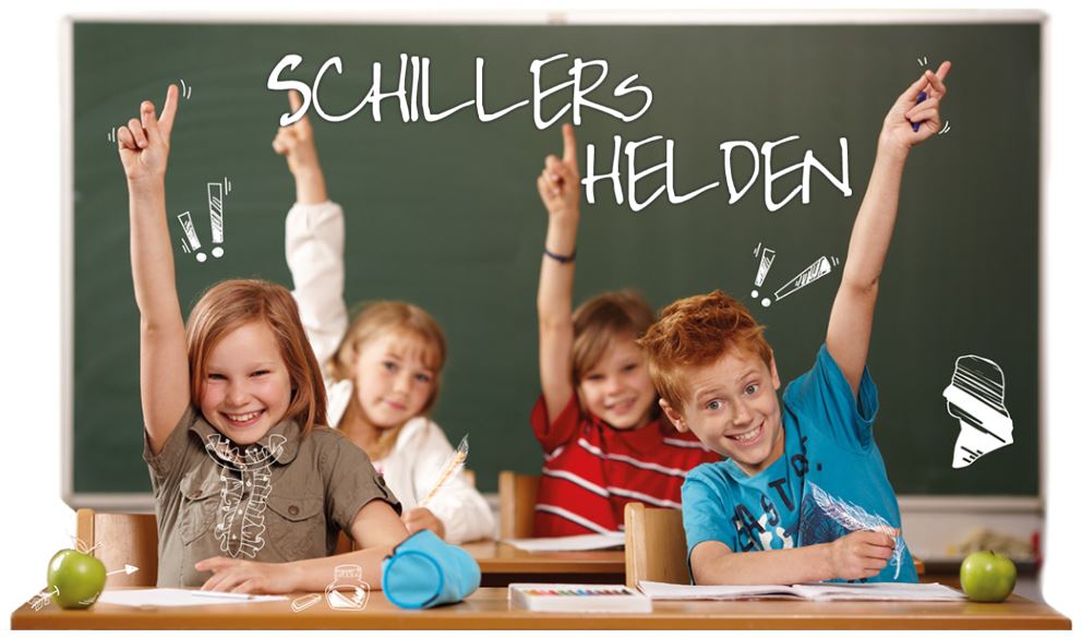 Schillerschule Spaichingen Fröhliche Schülergruppe sitzt im Klassenzimmer vor der Tafel. Auf der Tafel steht mit Kreide geschrieben, Schillers Helden.